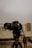 A Canon DSLR camera mounted on a Yunteng tripod is prominently displayed against a blurred urban background. The camera is facing forward and the image captures its lens and body in detail, emphasizing the professional equipment.