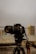 A Canon DSLR camera mounted on a Yunteng tripod is prominently displayed against a blurred urban background. The camera is facing forward and the image captures its lens and body in detail, emphasizing the professional equipment.