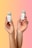 Two hands are holding small green beverage bottles labeled 'magic mind' against a gradient background that transitions from yellow to pink. The bottles have labels indicating ingredients such as matcha and honey. The nails on the hands are painted in different pastel colors.