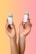 Two hands are holding small green beverage bottles labeled 'magic mind' against a gradient background that transitions from yellow to pink. The bottles have labels indicating ingredients such as matcha and honey. The nails on the hands are painted in different pastel colors.