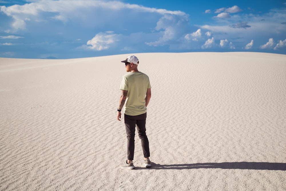man in green shirt and blue denim jeans standing on white sand during daytime