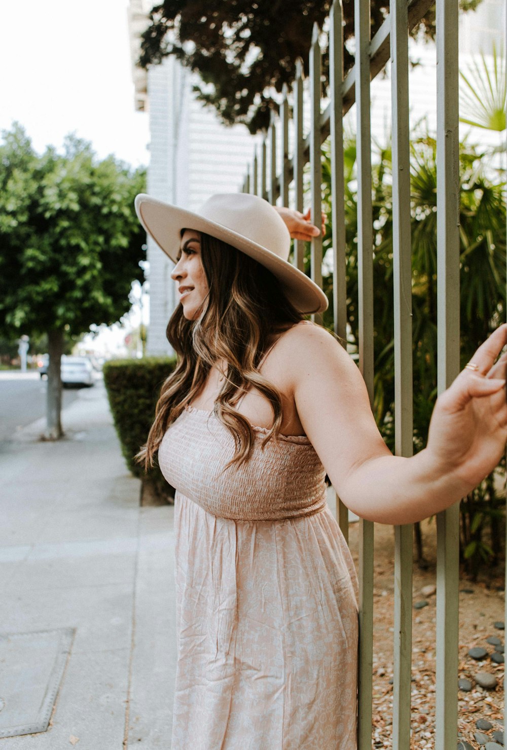 woman in beige sleeveless dress wearing white hat standing on sidewalk during daytime