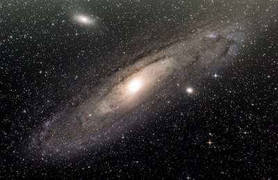 The image depicts a large spiral galaxy with a bright central nucleus surrounded by a diffuse halo of stars and dust. Numerous stars are scattered across the scene, twinkling against the dark backdrop of space. There are distinct spiral arms wrapping around the galaxy's core, creating a sense of depth and structure.