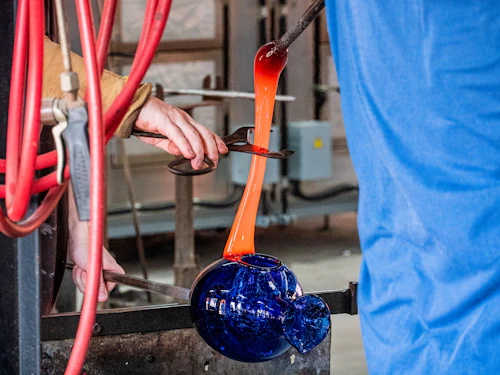 Hands shaping molten glass over a torch