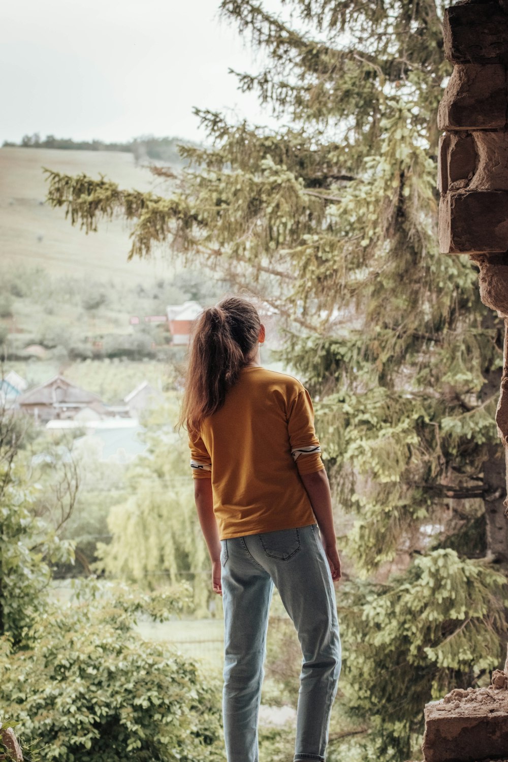 woman in orange shirt and blue denim jeans standing on rock formation during daytime