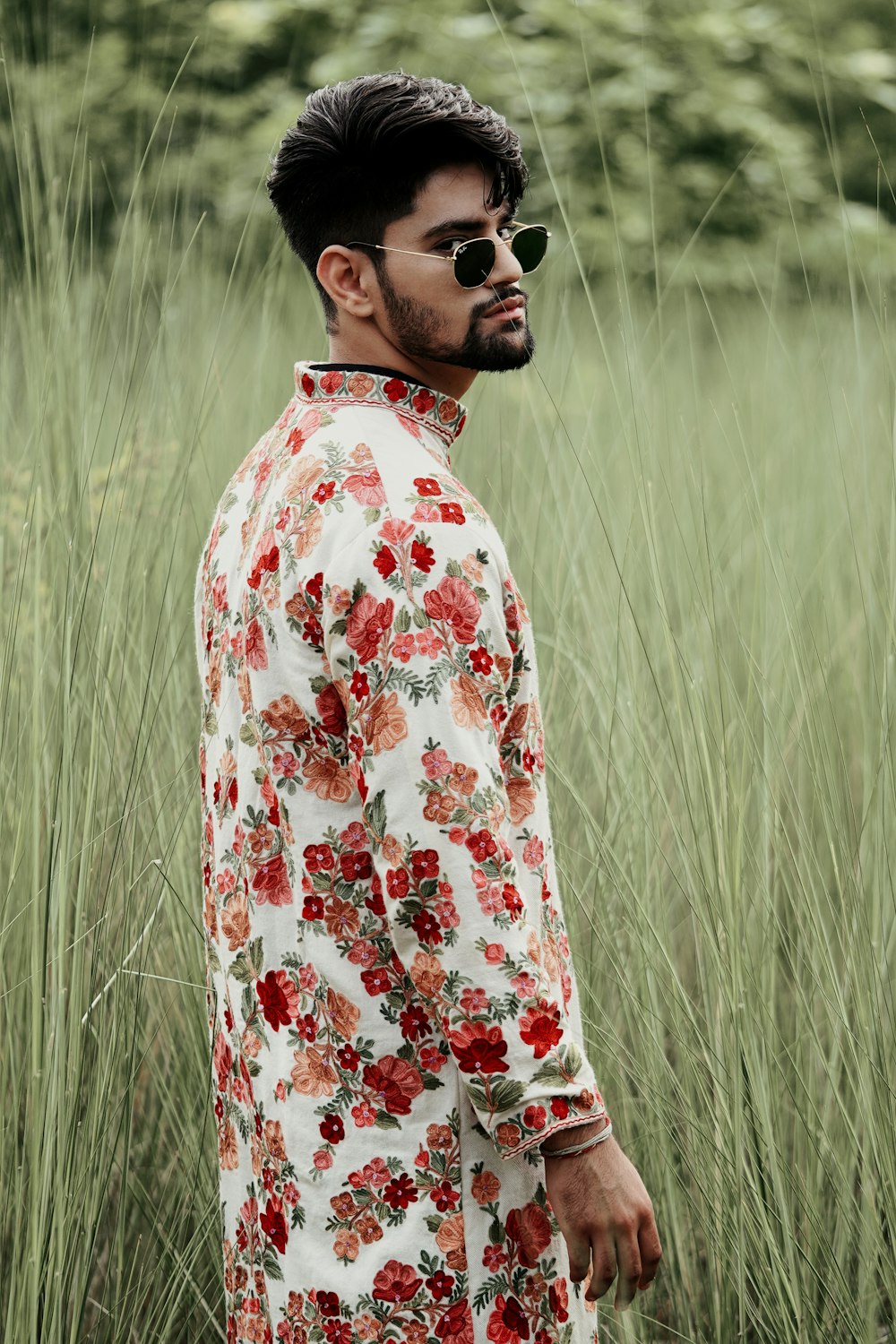 man in white red and blue floral dress shirt wearing black sunglasses standing on green grass