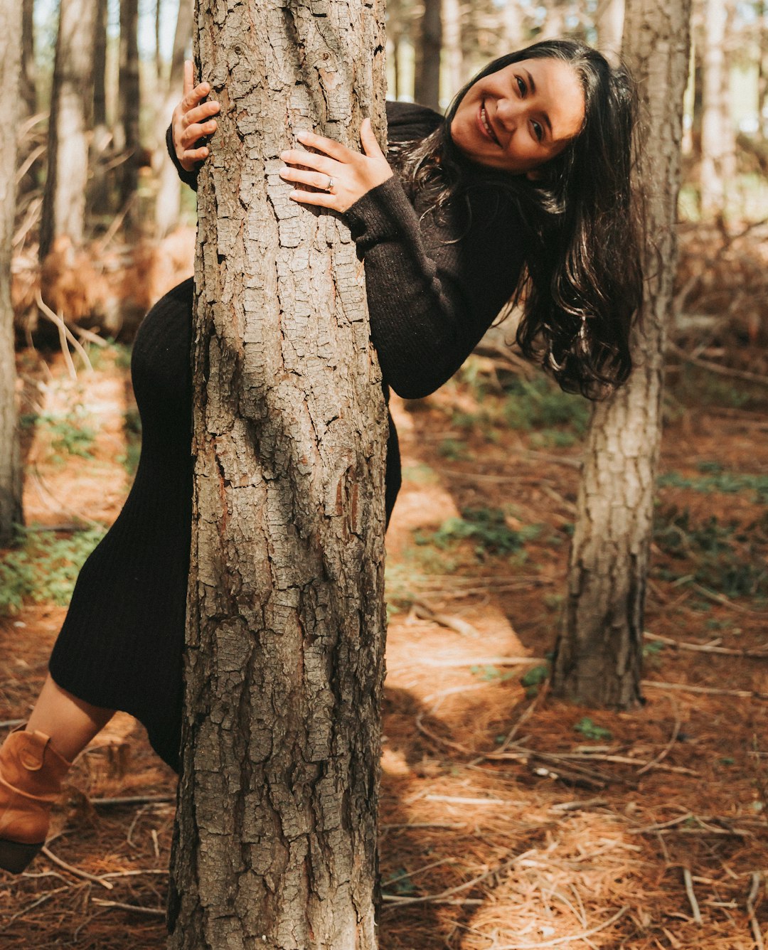 woman in black dress leaning on brown tree