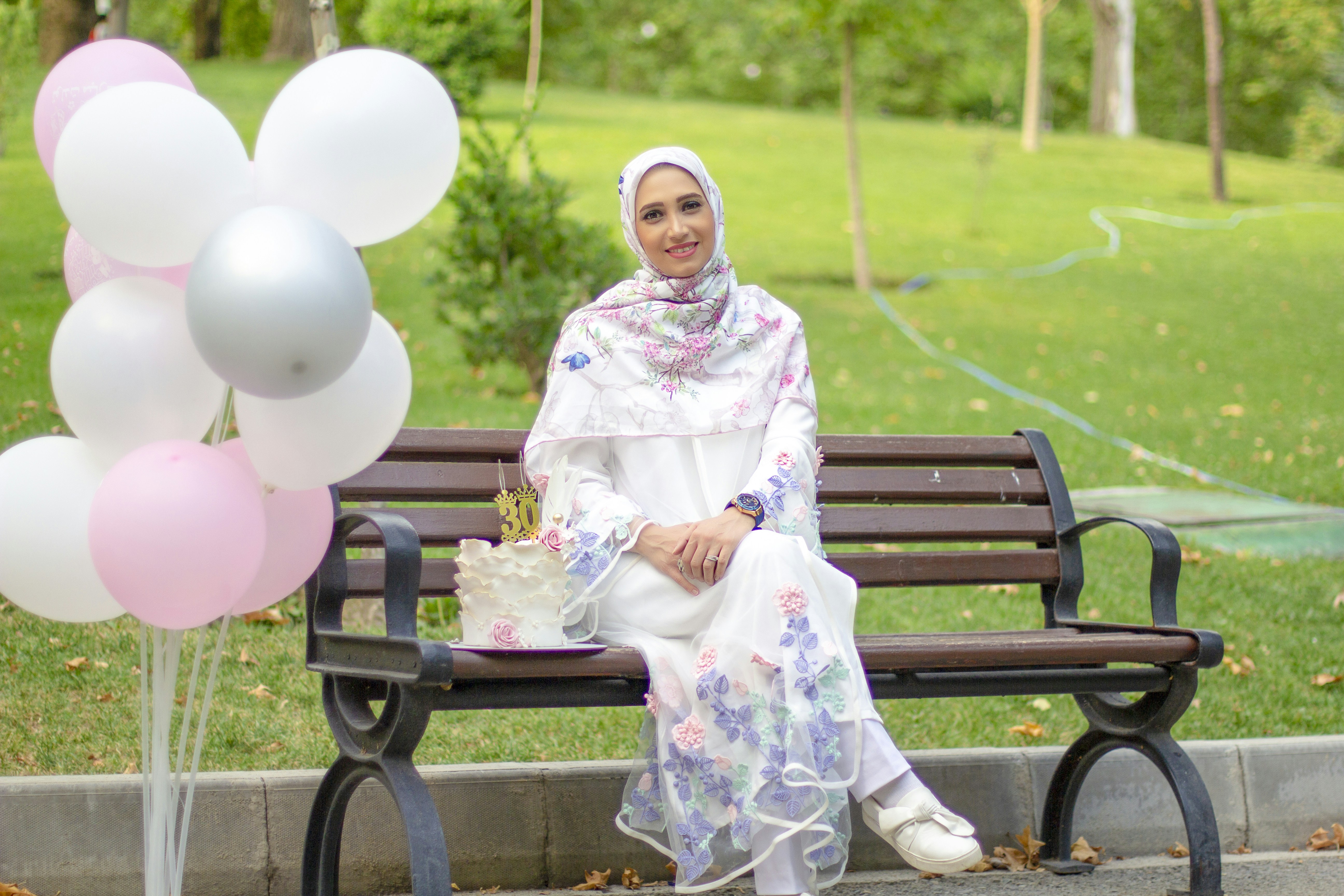 woman in white and pink floral hijab sitting on brown wooden bench