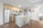 A modern kitchen with a minimalist design featuring stainless steel appliances, including a refrigerator, oven, and microwave. Light wood cabinets complement the sleek white countertops. A central island with a sink has two wooden barstools with metal legs. Decorative plates hang on a white wall, and wood flooring adds warmth to the space.