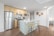 A modern kitchen with a minimalist design featuring stainless steel appliances, including a refrigerator, oven, and microwave. Light wood cabinets complement the sleek white countertops. A central island with a sink has two wooden barstools with metal legs. Decorative plates hang on a white wall, and wood flooring adds warmth to the space.