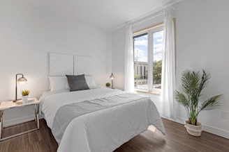 A serene bedroom corner with linen bedding and a small indoor plant by the window.