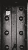 A close-up view of a metallic surface with large rivets or bolts. There is a small grid-marked paper or sticker with a target-like symbol and the letters L and A on it. The texture of the metal is rough and worn.