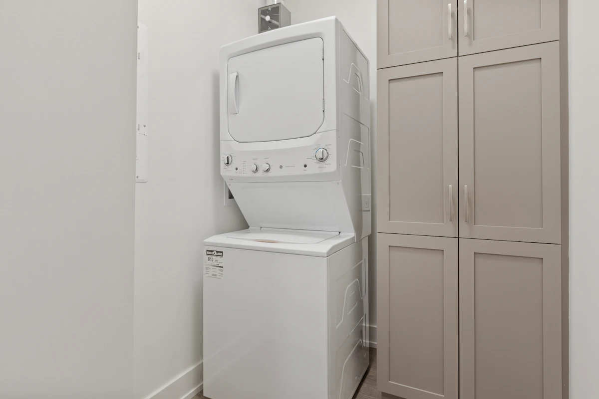 Colonne lave-linge et sèche-linge superposés dans une buanderie étroite aux murs blancs