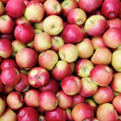 A large pile of fresh apples with a mix of red and green colors, tightly packed together. The apples vary slightly in size and have smooth, shiny skins.