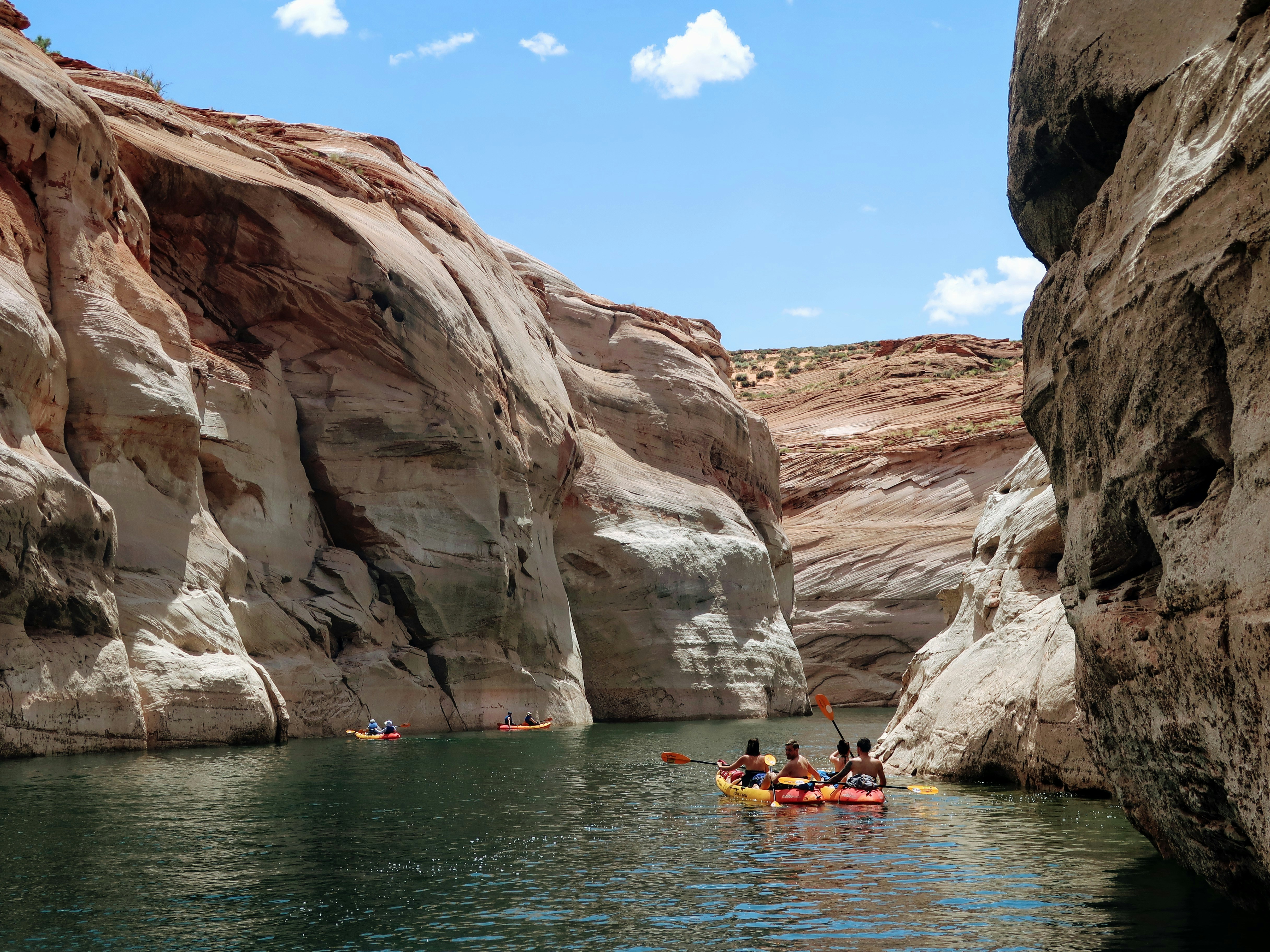 people riding on kayak on sea near brown rock formation during daytime