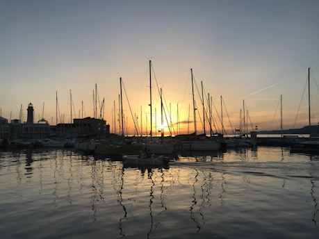 Sunset over Mount Maunganui harbor with sleek sailboats moored near the coast.