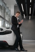 man in black suit jacket and pants standing beside white car