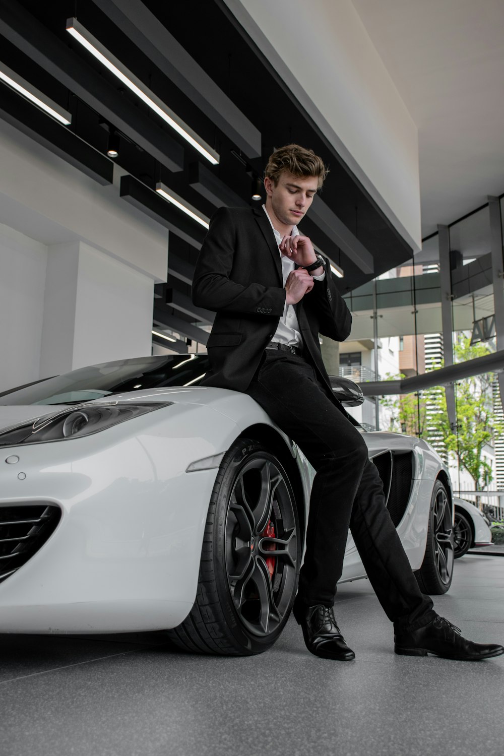 hombre con traje negro de pie junto a un coche blanco