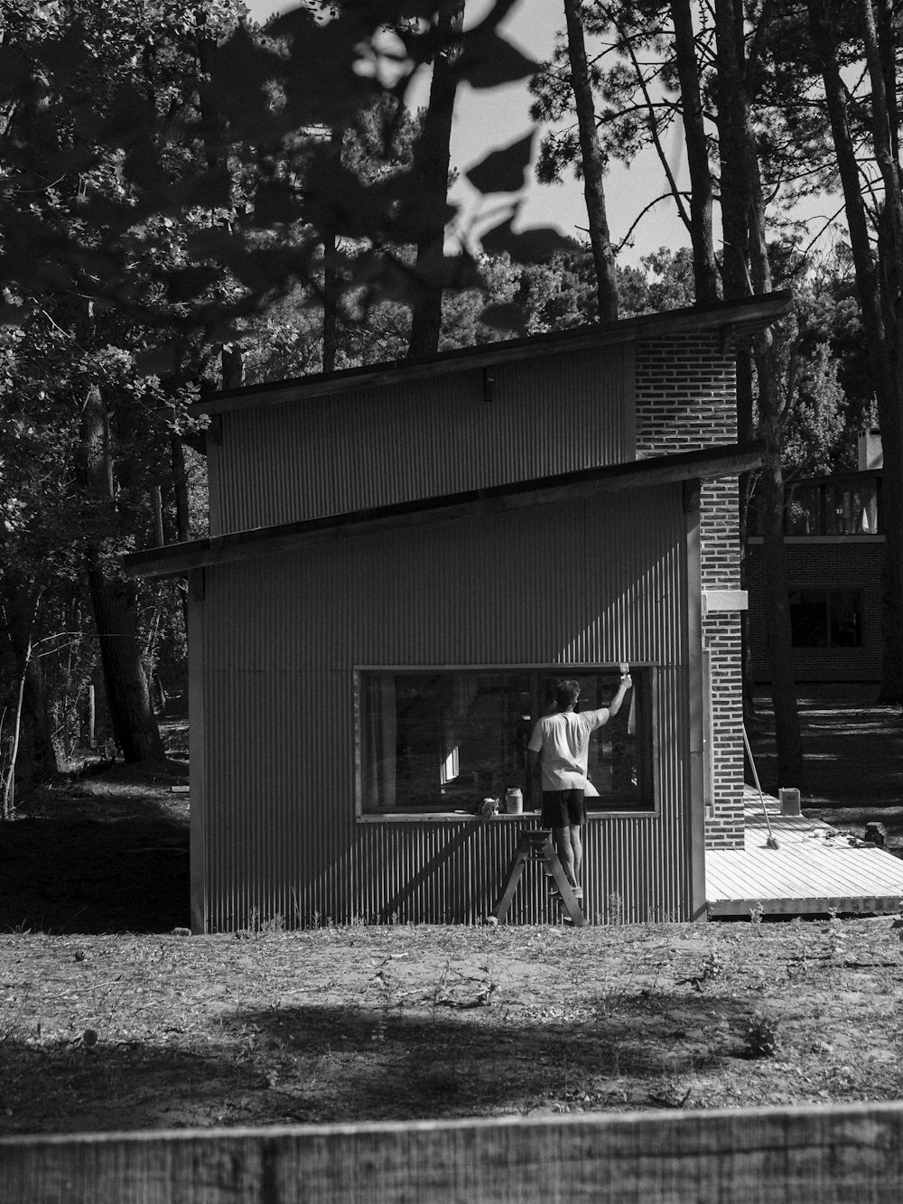 grayscale photo of man sitting on bench near house