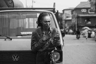 A Latina woman courier checking a digital device while standing next to a medical van in a city setting.