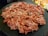 A pile of thinly sliced marinated meat is spread out on a dark round platter, with visible marbling and reddish hues.