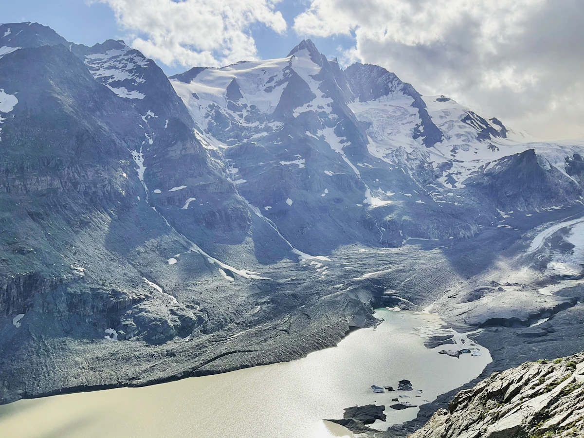 The Grossglockner above a glacier and its milky meltwater lake, under broken cloud