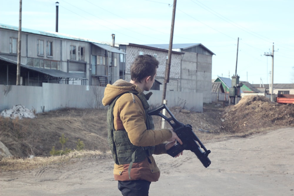 man in brown jacket holding black rifle