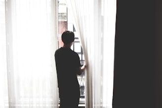 a man standing in front of a window looking out