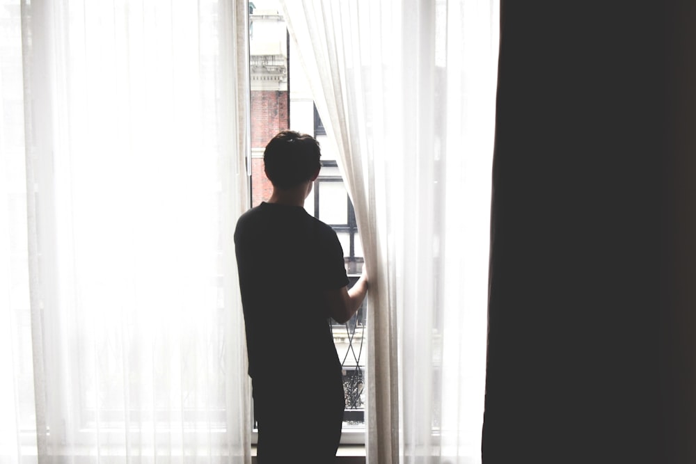 窓の前に立って外を眺める男