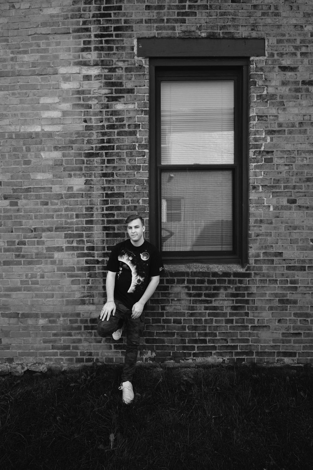 a man leaning against a brick wall next to a window