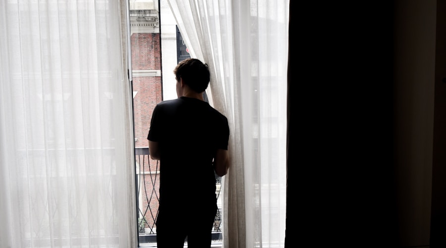 man in black crew neck t-shirt standing near white window curtain