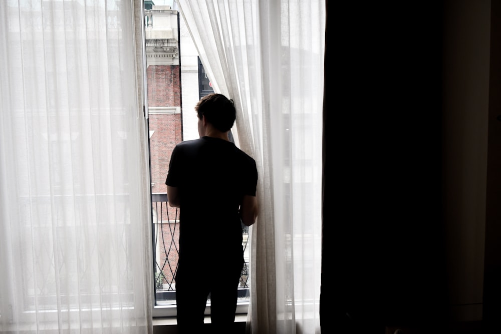 man in black crew neck t-shirt standing near white window curtain