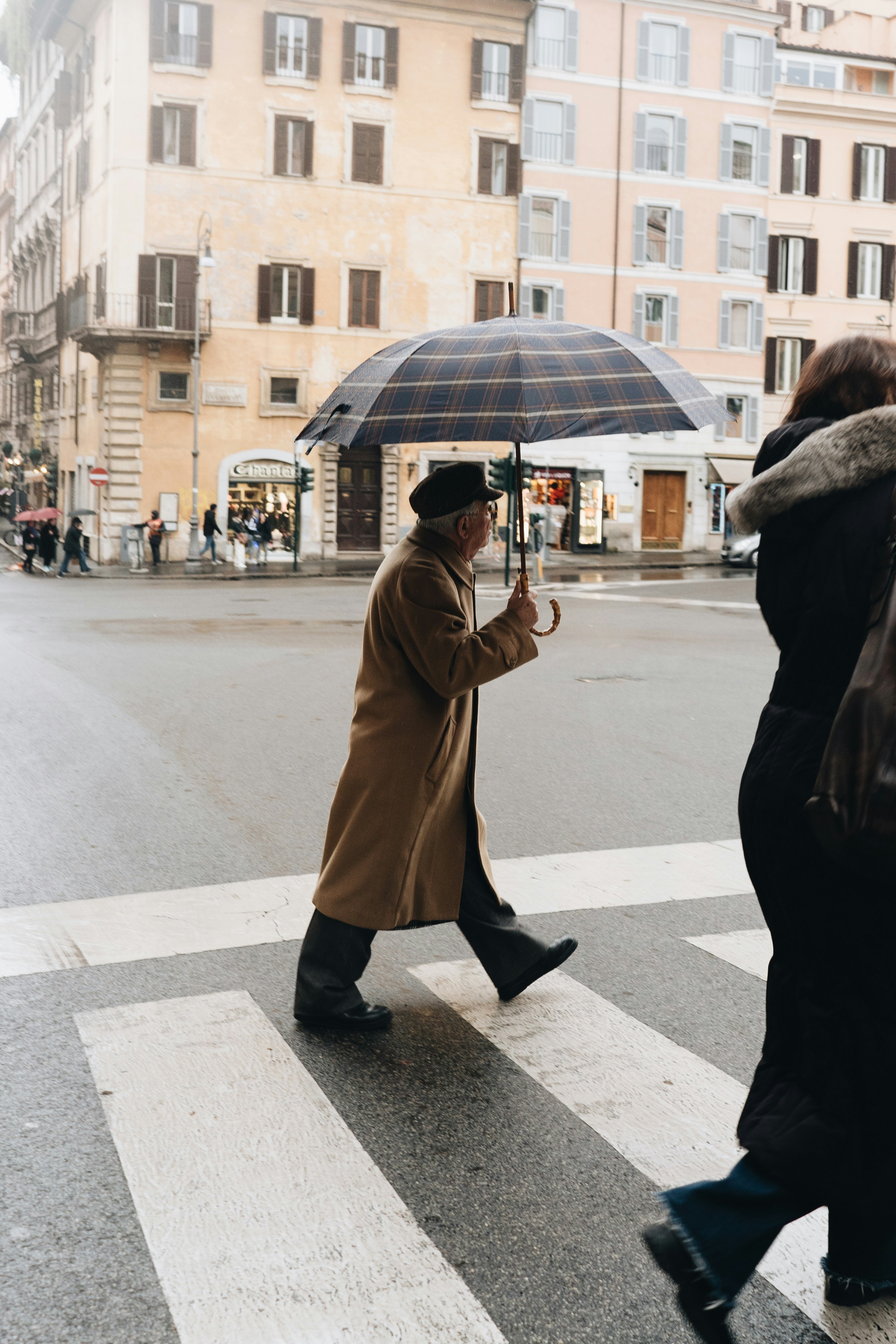 woman in brown coat holding umbrella walking on sidewalk during daytime