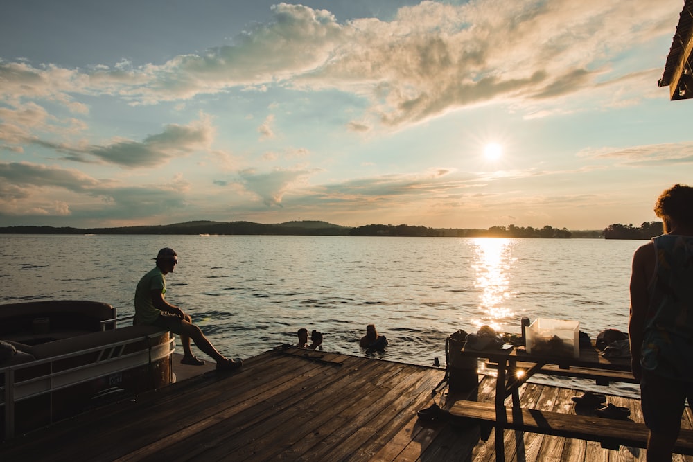 man and woman sitting on brown wooden dock during sunset