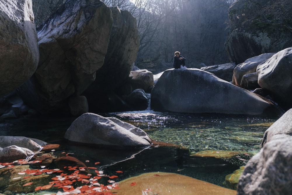 昼間、川の近くの岩の上に座る黒いジャケットを着た男