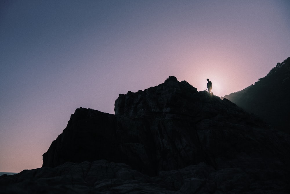 silhouette of person standing on rock formation during sunset
