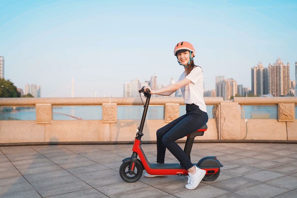 woman in white shirt and blue denim jeans riding red and white kick scooter during daytime