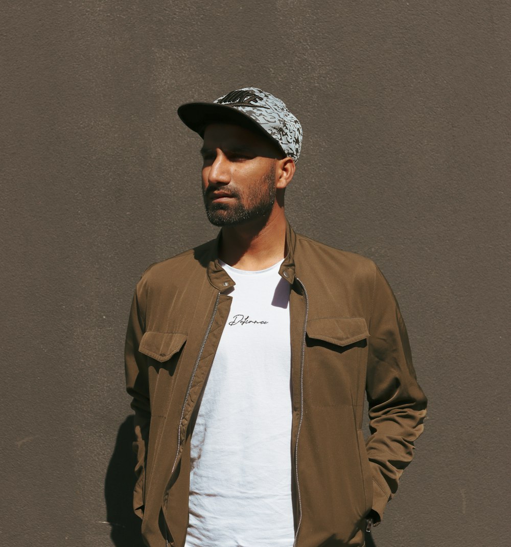 man in brown coat and black hat standing beside brown wall