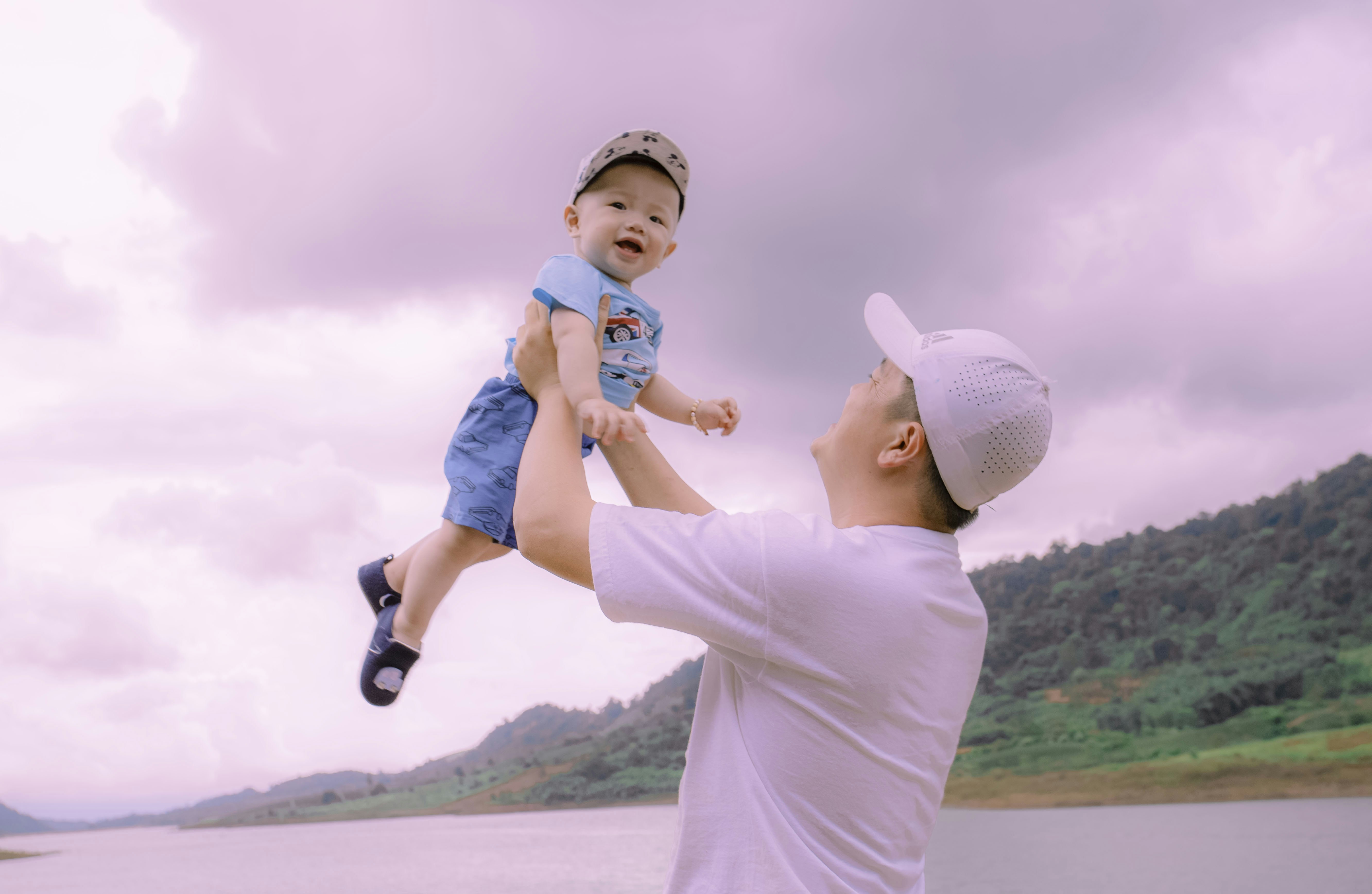 Anak laki-laki dengan kemeja lengan panjang putih membawa bayi dengan onesie biru