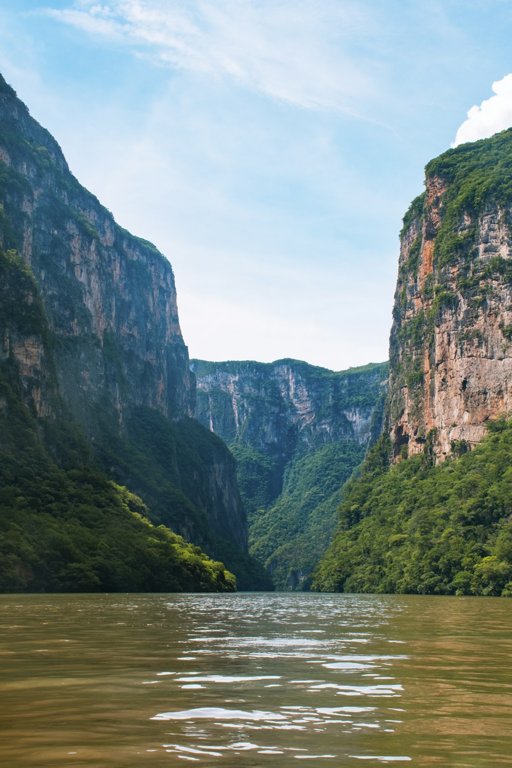 montanha verde e marrom ao lado do corpo de água durante o dia