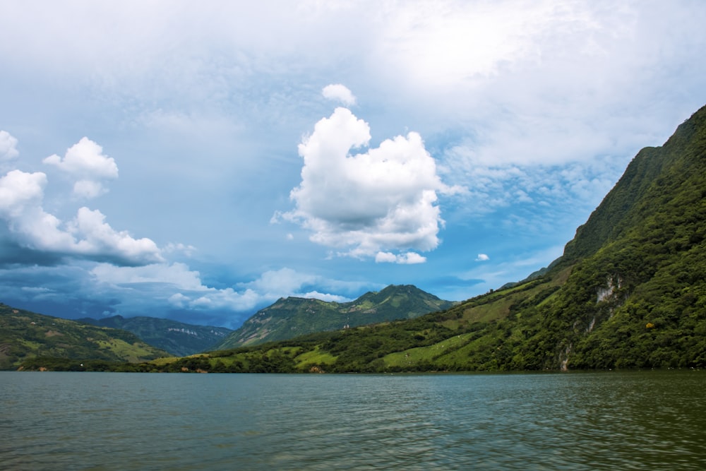 Grüner Berg neben Gewässer unter blauem Himmel und weißen Wolken tagsüber