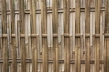 An arrangement of vertical and horizontal bamboo sticks forms a traditional woven fence. The bamboo appears natural and untreated with variations in color and texture, giving it a rustic yet organized look.