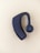 A black Bluetooth earpiece with a sleek design is placed on a light beige background. The earpiece has an ergonomic shape with a circular speaker grill featuring a concentric pattern.