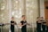A group of women practicing martial arts in a well-lit room, each holding a wooden or bamboo training weapon. They are wearing matching black attire and appear focused and coordinated, suggesting a structured training session.