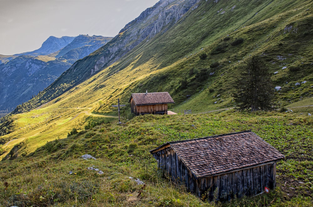 brown wooden house on green grass field near green mountains during daytime