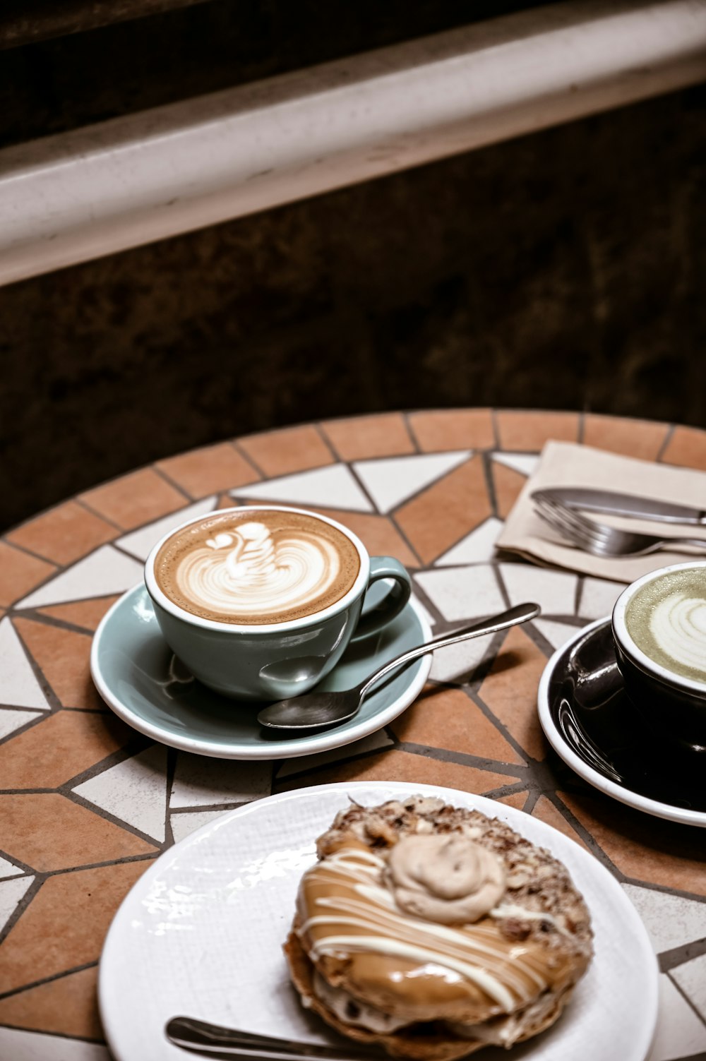 cappuccino in white ceramic cup on saucer beside stainless steel spoon on table