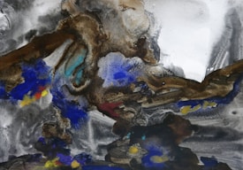 Abstract image featuring swirling patterns of earthy browns, vivid blues, and subtle hints of yellow set against a smoky gray backdrop. The texture appears rich, resembling layers of watercolor or ink washes merging into a fluid composition.