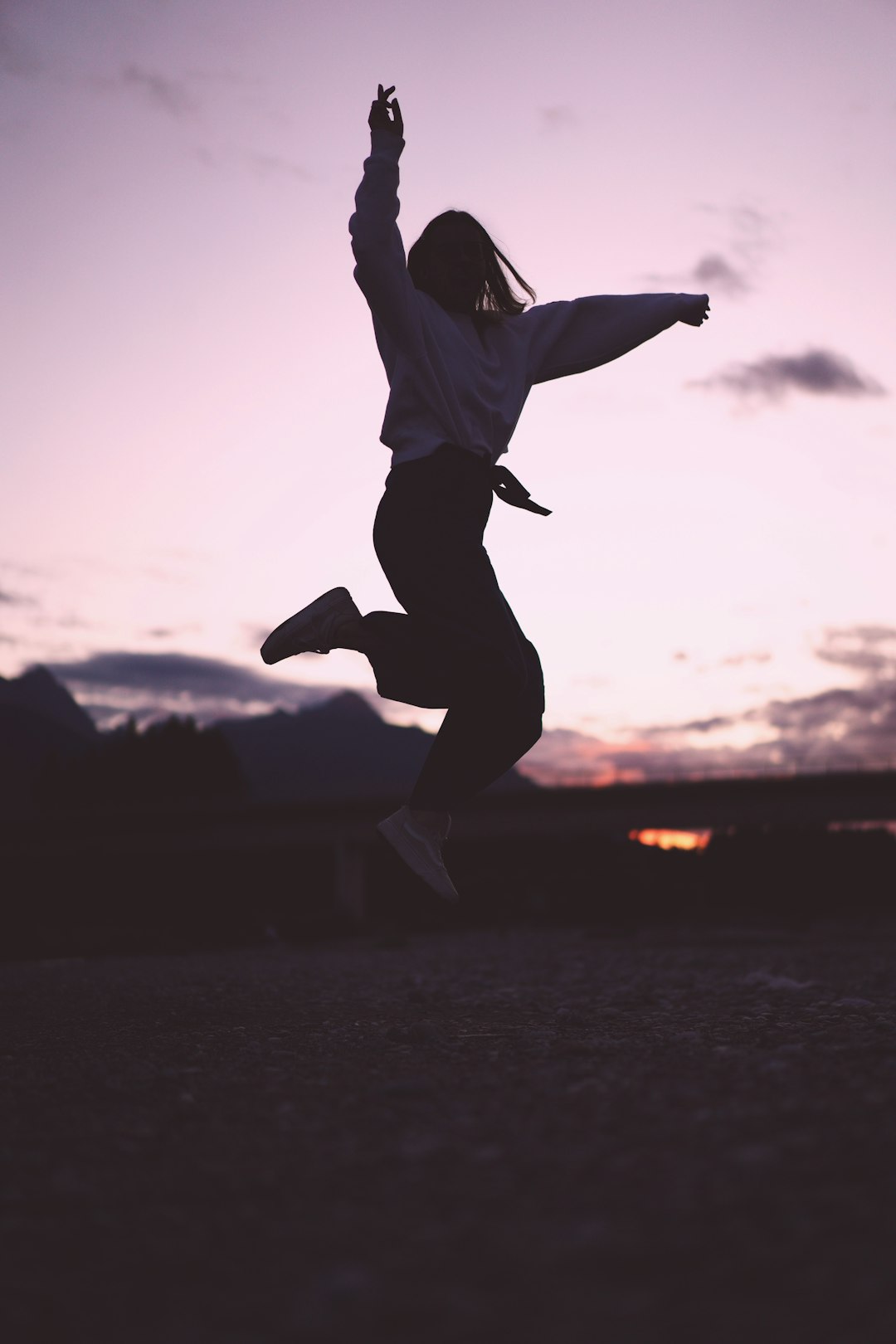 woman in white shirt and black pants jumping on mid air during sunset