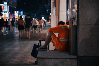man in orange hoodie sitting on concrete bench