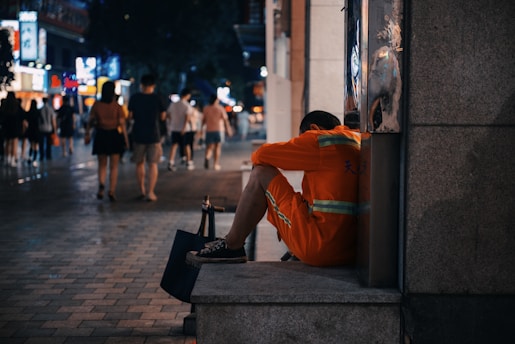 man in orange hoodie sitting on concrete bench